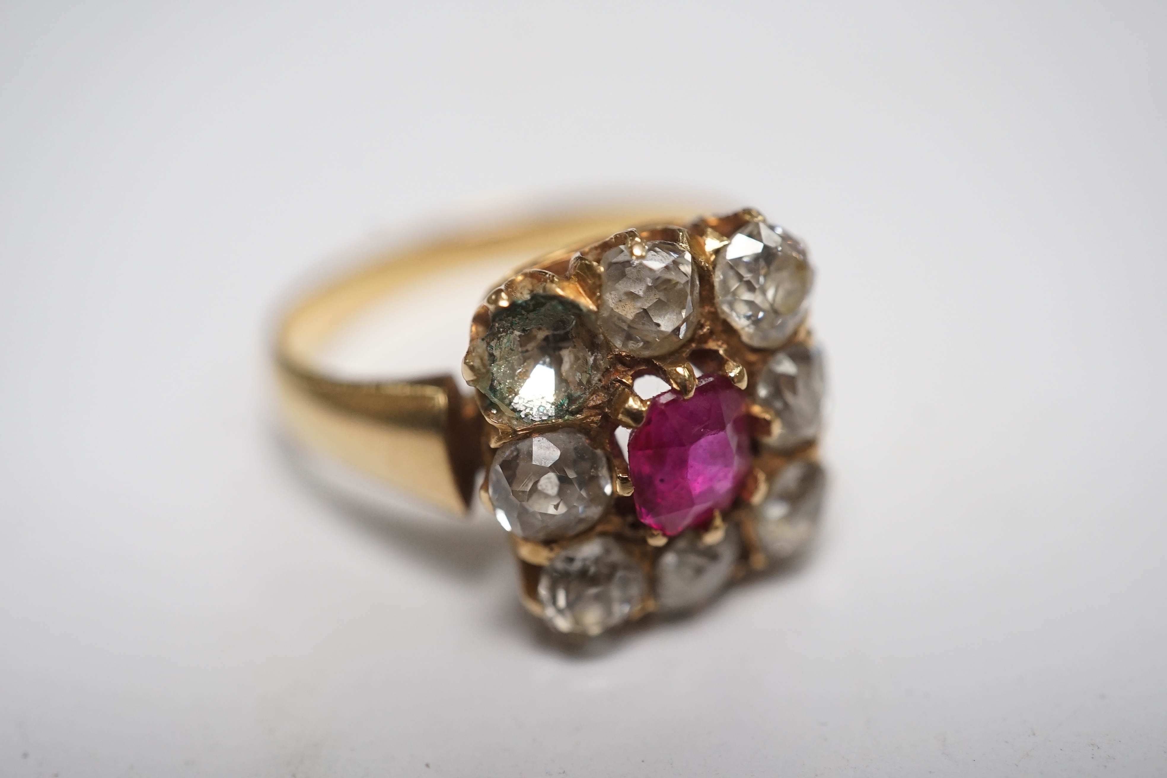 An early 20th century yellow metal, single stone ruby and eight stone diamond set square cluster ring, size O, gross weight 5 grams, one diamond missing. Condition - poor to fair